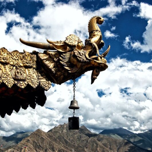Vergoldeter Drachenkopf auf dem Dach eines tibetischen Klosters vor der Berglandschaft des Himalayas.