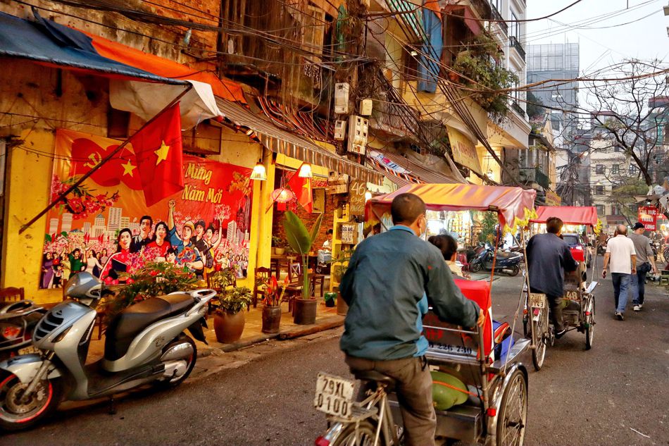 Lebhafte Straße mit Geschäften und Fahrradrikscha in Hanoi